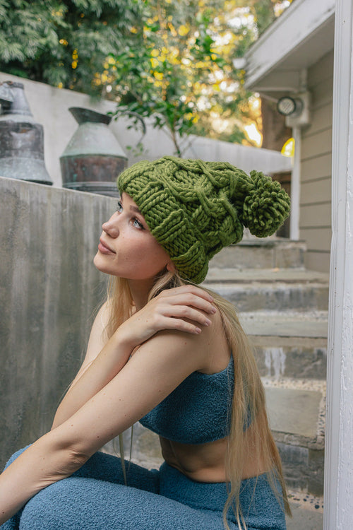 Woman wearing a green knitted beanie sitting on steps outdoors.