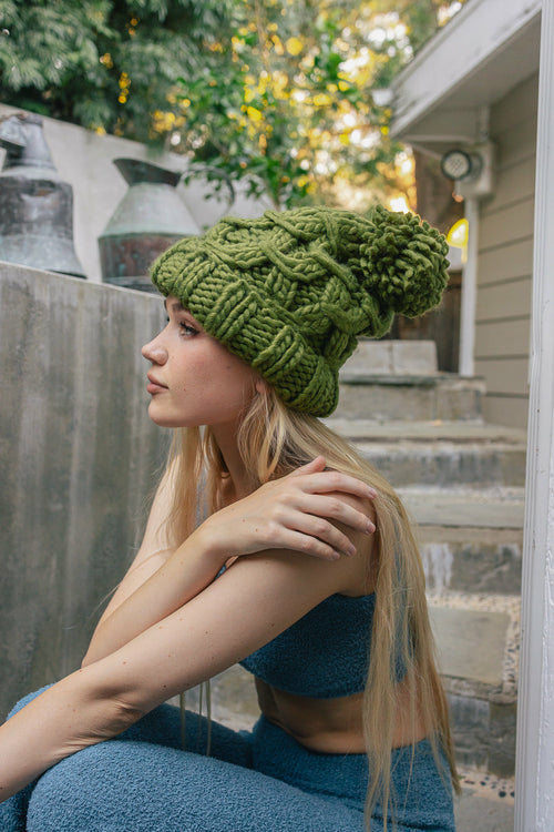 Woman wearing a green knitted hat sitting on steps outdoors.