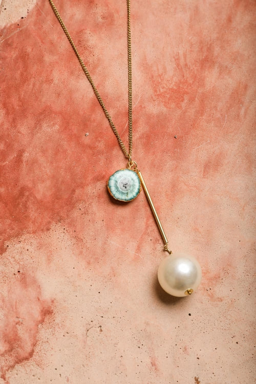 Necklace with a pendant and pearl on a textured pink surface