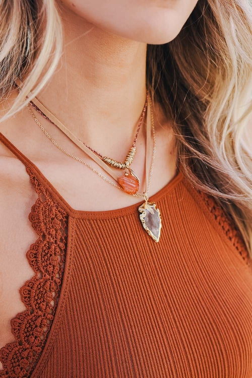 Close-up of a person wearing multiple necklaces with a brown top.