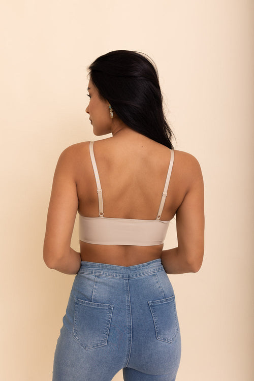 Woman wearing a beige bralette and blue jeans against a beige background
