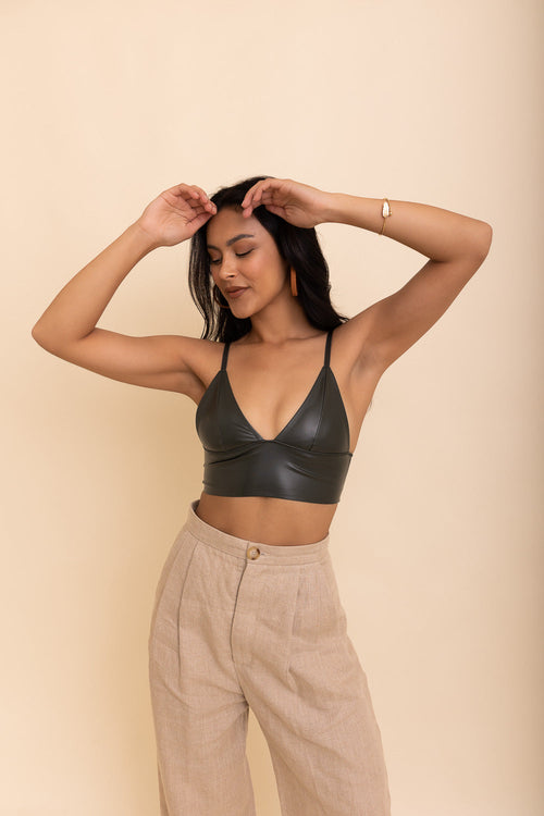 Woman wearing a black leather top and beige pants against a beige background