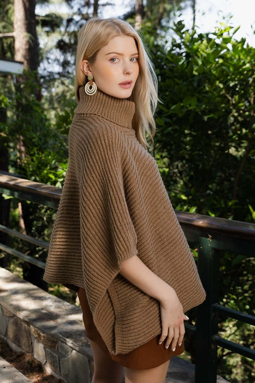 Woman wearing a brown poncho outdoors with greenery in the background