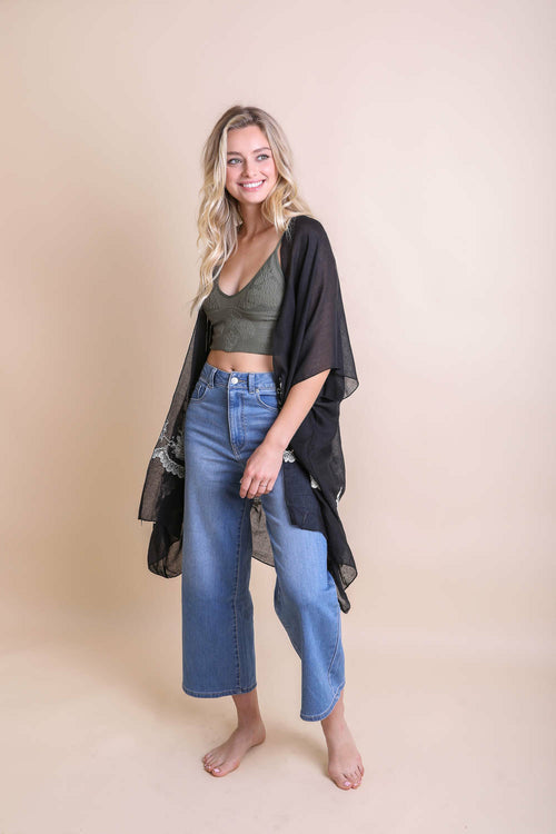 Woman wearing a green crop top, blue jeans, and a black shawl on a beige background