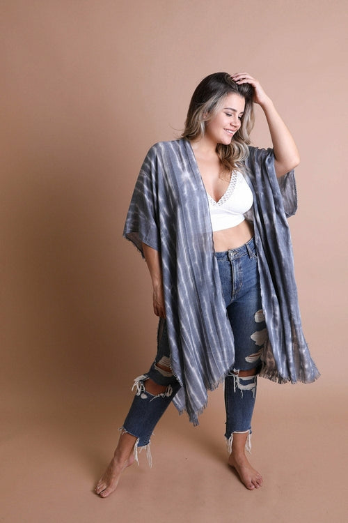 Woman wearing a gray kimono over a white top and jeans on a beige background