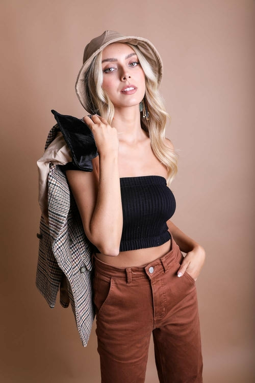 Woman wearing a black tube top, brown pants, and a beige hat against a beige background