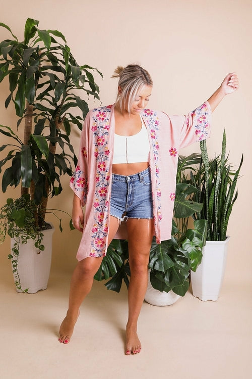 Woman wearing a floral kimono standing among potted plants on a beige background