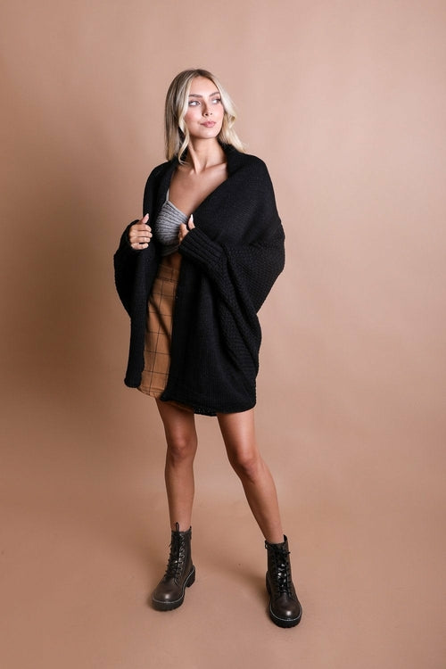 Woman wearing a black oversized sweater and brown boots on a beige background