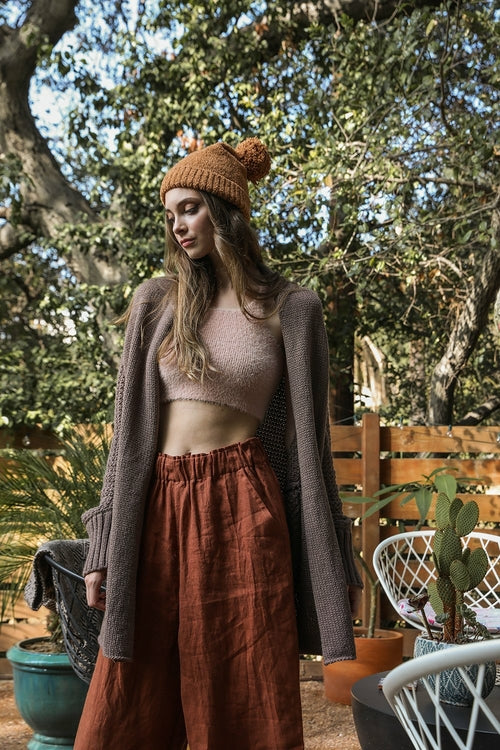 Woman wearing a brown beanie and cardigan outdoors with trees in the background