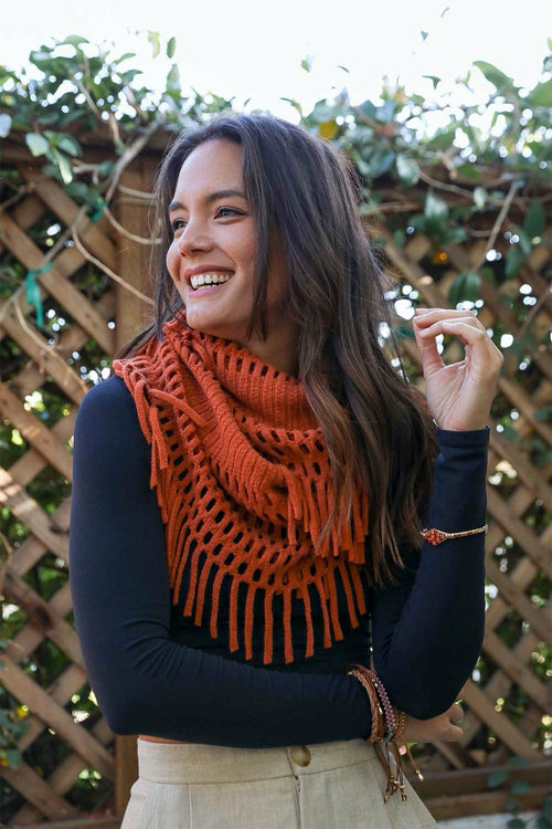 Woman wearing an orange scarf with a wooden fence and greenery in the background