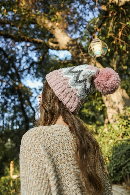 Person wearing a patterned knit beanie with a pom-pom in an outdoor setting