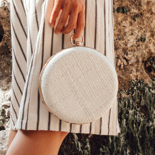 Person holding a round woven handbag with a striped dress in the background