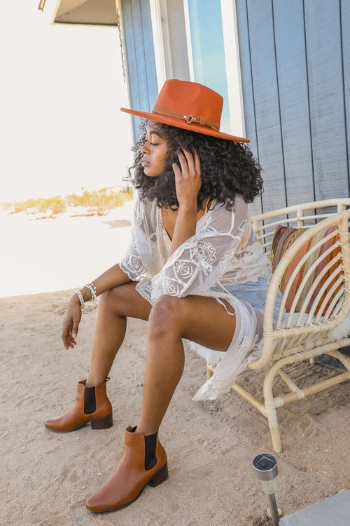 Woman sitting on a beach chair wearing a white lace cover-up, orange hat, and brown boots.