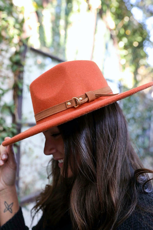 Person wearing a rust-colored wide-brimmed hat with a brown band outdoors.