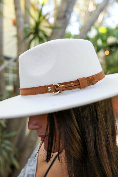 White hat with a brown band worn by a person, with a blurred natural background
