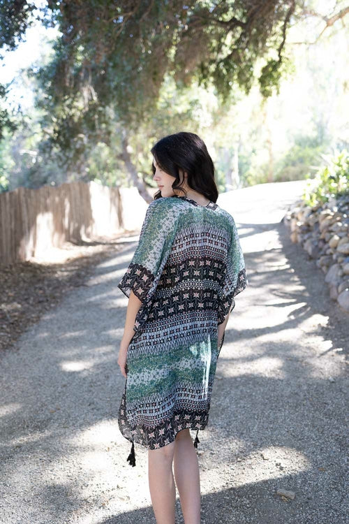 Woman wearing a patterned dress walking on a path with trees and sunlight in the background
