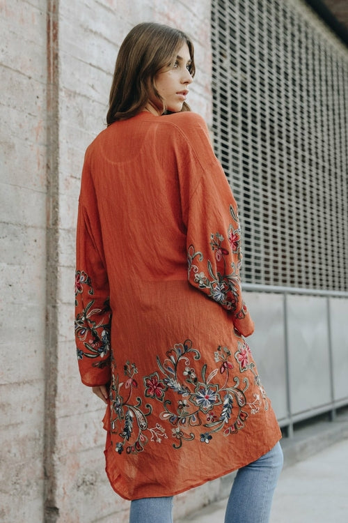 Woman wearing an orange embroidered dress against a textured wall.