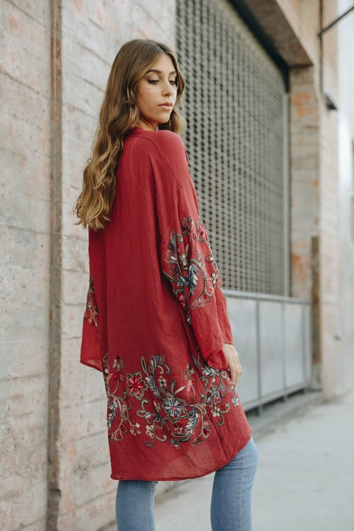 Woman wearing a red embroidered kimono against a brick wall.