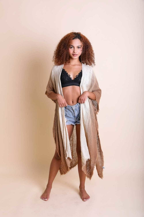 Woman wearing a kimono over a black bra and denim shorts on a beige background