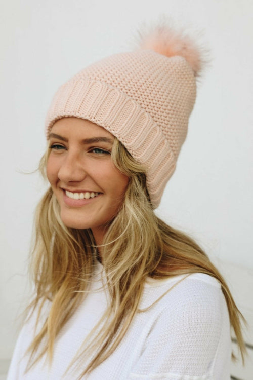 Woman wearing a pink knit beanie with a pom-pom against a white background