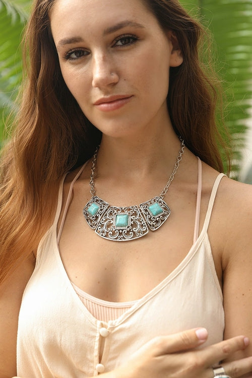 Woman wearing a decorative necklace with turquoise stones against a blurred green background