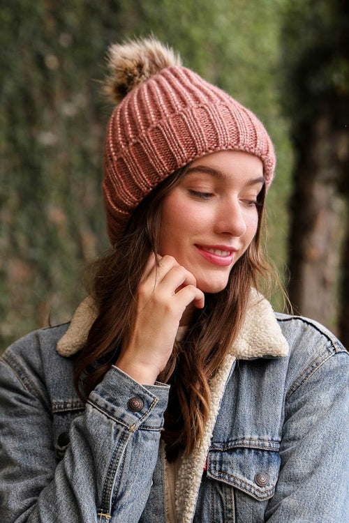 Woman wearing a pink knit beanie with a pom-pom outdoors