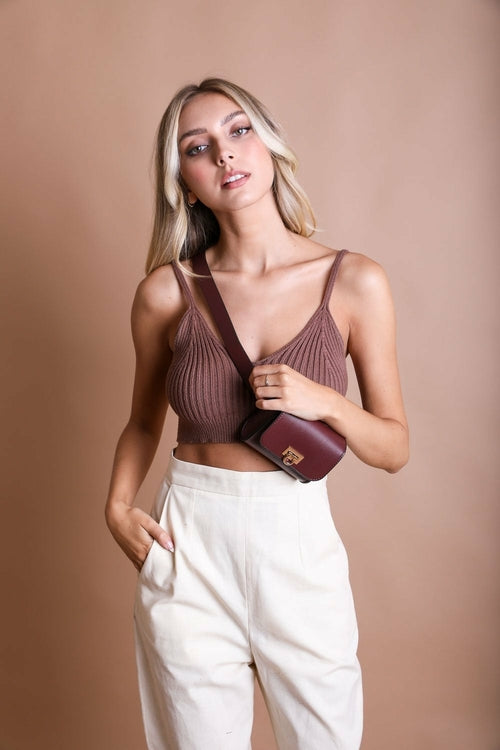 Woman wearing a brown textured top and white pants against a beige background
