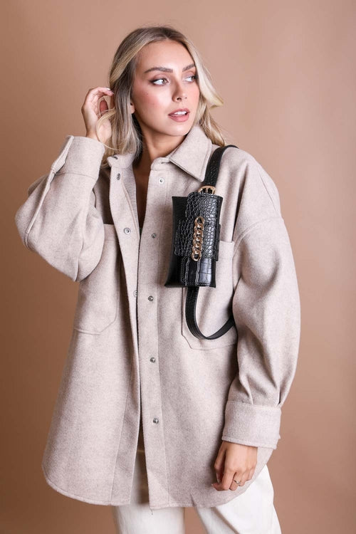 Woman wearing a beige coat holding a black handbag against a brown background